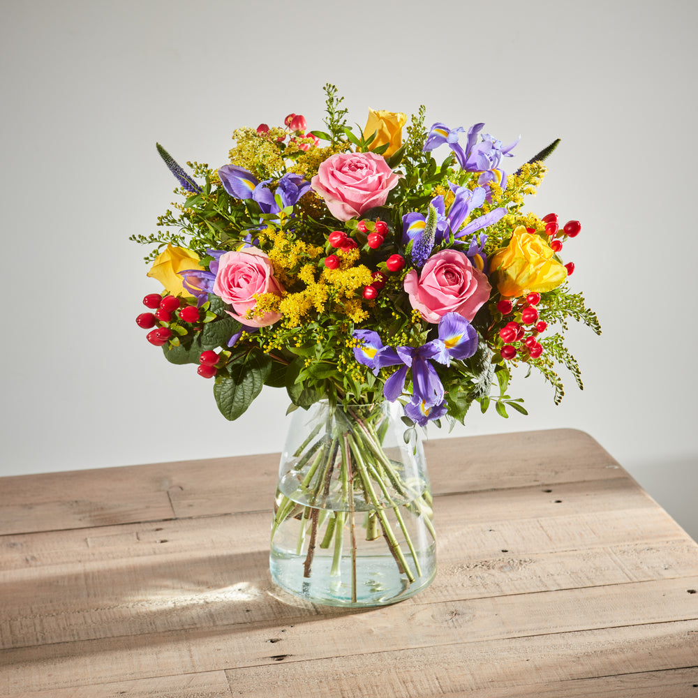 FVibrant mixed flower bouquet featuring pink roses, purple irises, and yellow solidago.